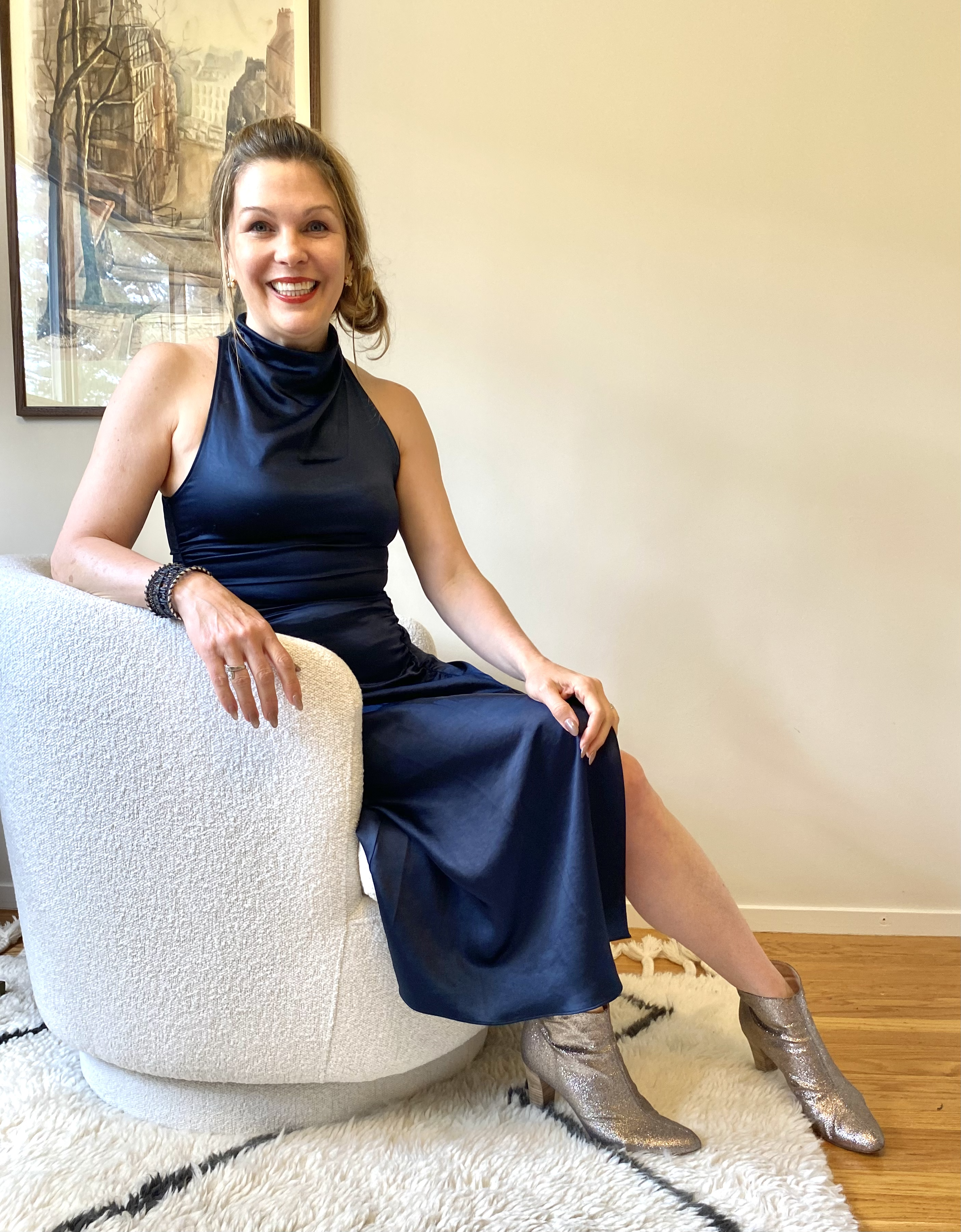 Dr Backos in a blue dress, sitting on a chair smiling.
